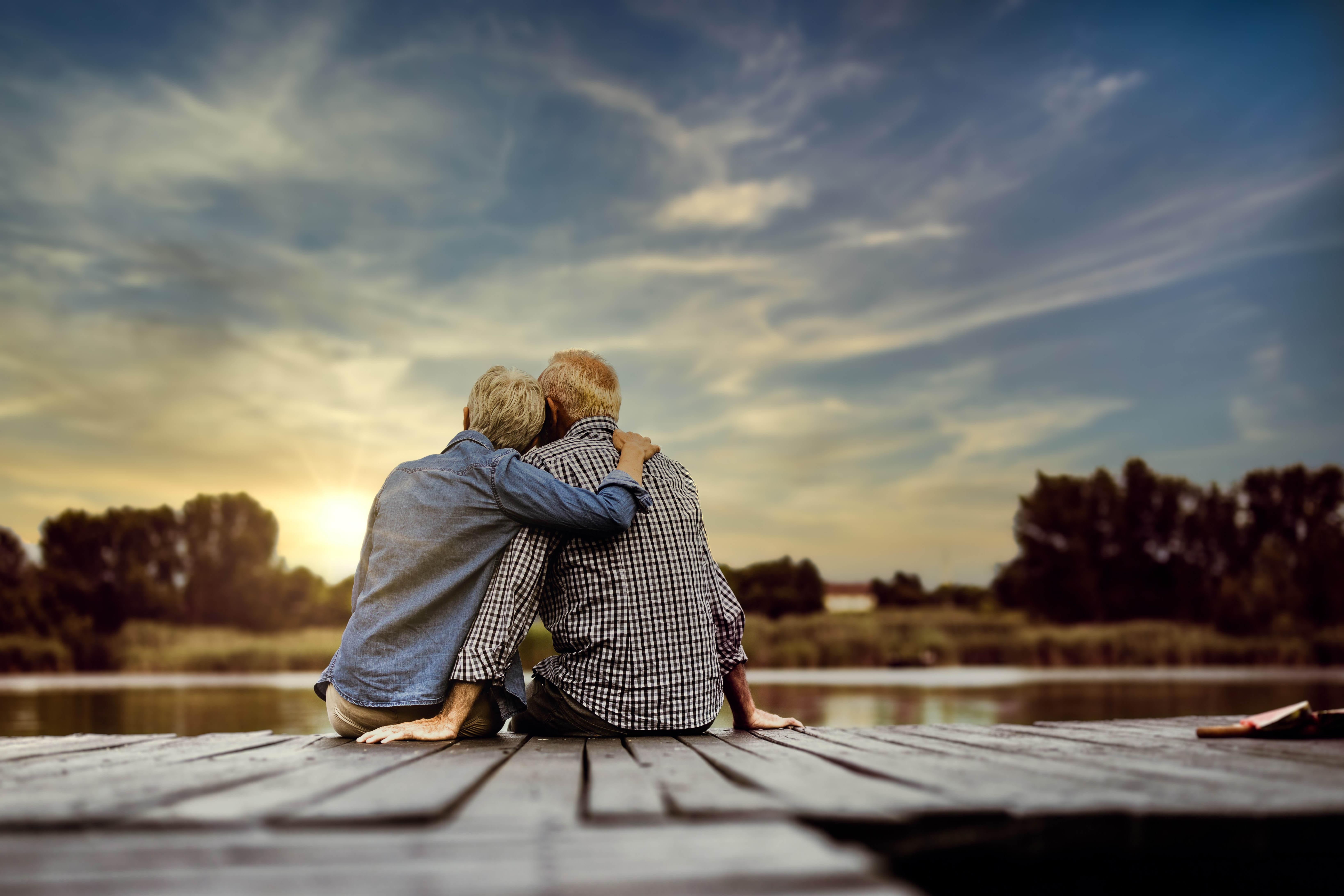 Rear view of a loving senior couple on a pier at river.